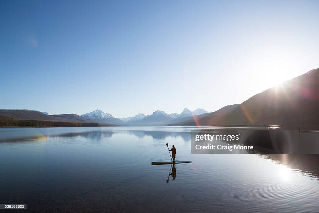 A man stand up paddle boards (SUP) on a calm Lake McDonald in Glacier National Park.