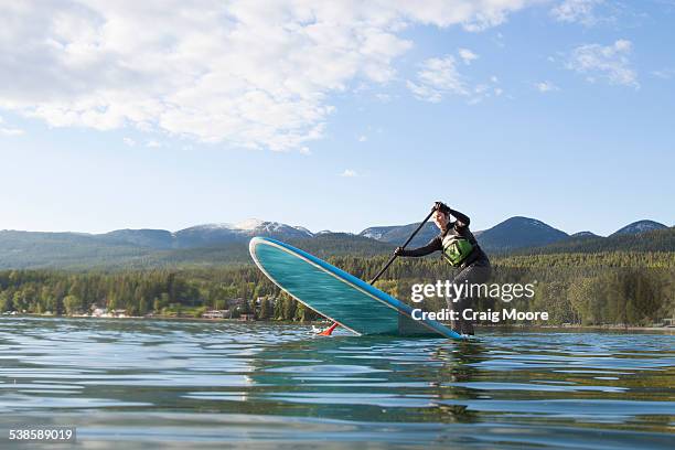 a fit female stand up paddle boards during the spring on whitefish lake in montana. - whitefish lake stock pictures, royalty-free photos & images