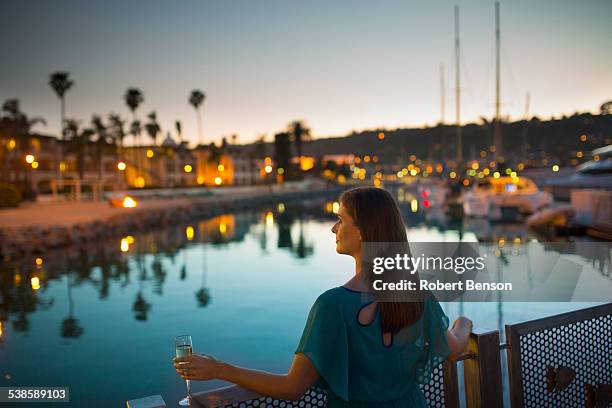 a pretty young girl with a drink in her left hand stands by the marina iron railing. - marina stock pictures, royalty-free photos & images