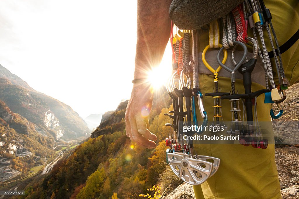 Various climbing gear including friends and nuts hanging on a climbers harness, backlit by the sun. Cadarese, Ossola, Italy.