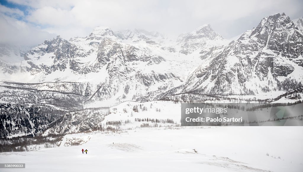 Two alpinists climb on a slope above the Valley of Devero in a stormy day with Cervandone group in background. Baceno, Piemonte, Italy.