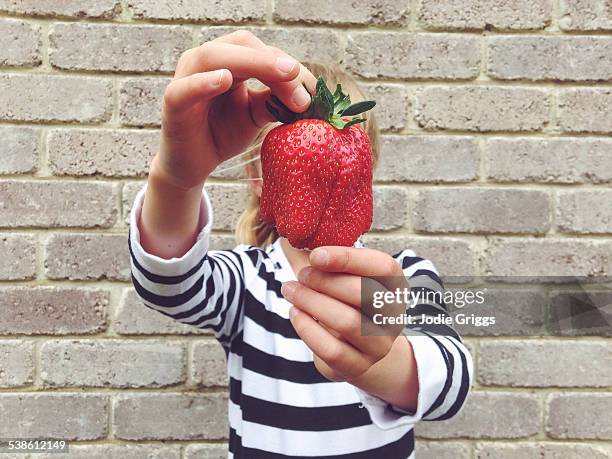 child holding large strawberry in front of face - perspective artificielle photos et images de collection