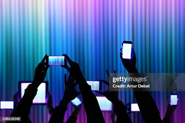 people raise his bright smartphone and tablet device during a night show celebration with dark silhouettes and colorful background. - addiction photos et images de collection