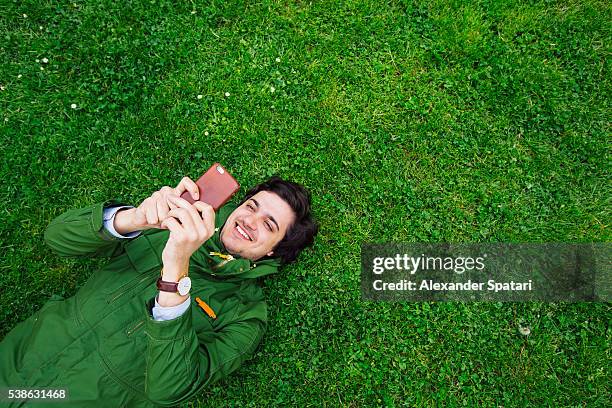 cheerful smiling young man lying on grass with smartphone - satisfied students stockfoto's en -beelden