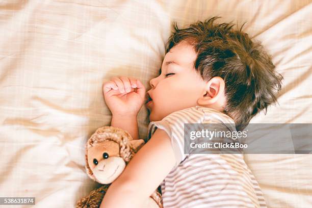 boy sleeping on bed holding a soft toy by his side - peuter stockfoto's en -beelden