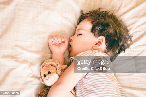 Boy sleeping on bed holding a soft toy by his side Boy sleeping on bed holding a soft toy by his side
