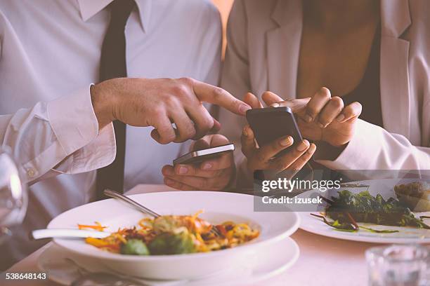 businessman and businesswoman using phones on lunch - global leadership dinner stock pictures, royalty-free photos & images