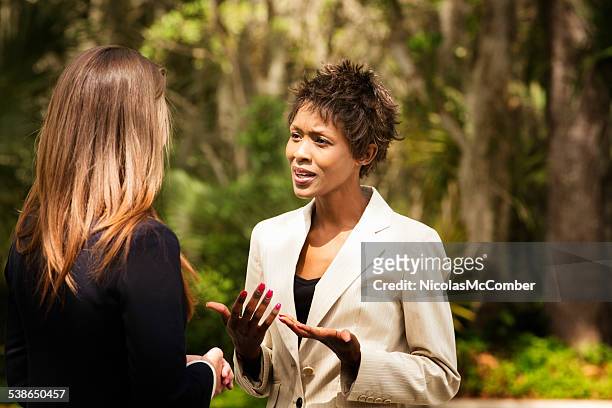 black female office worker explaining herself to colleague outdoors - angry coworker stock pictures, royalty-free photos & images