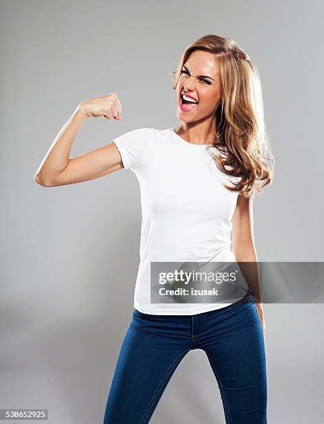 contente jovem mulher dobrando seu bíceps, retrato de estúdio - white t shirt studio imagens e fotografias de stock