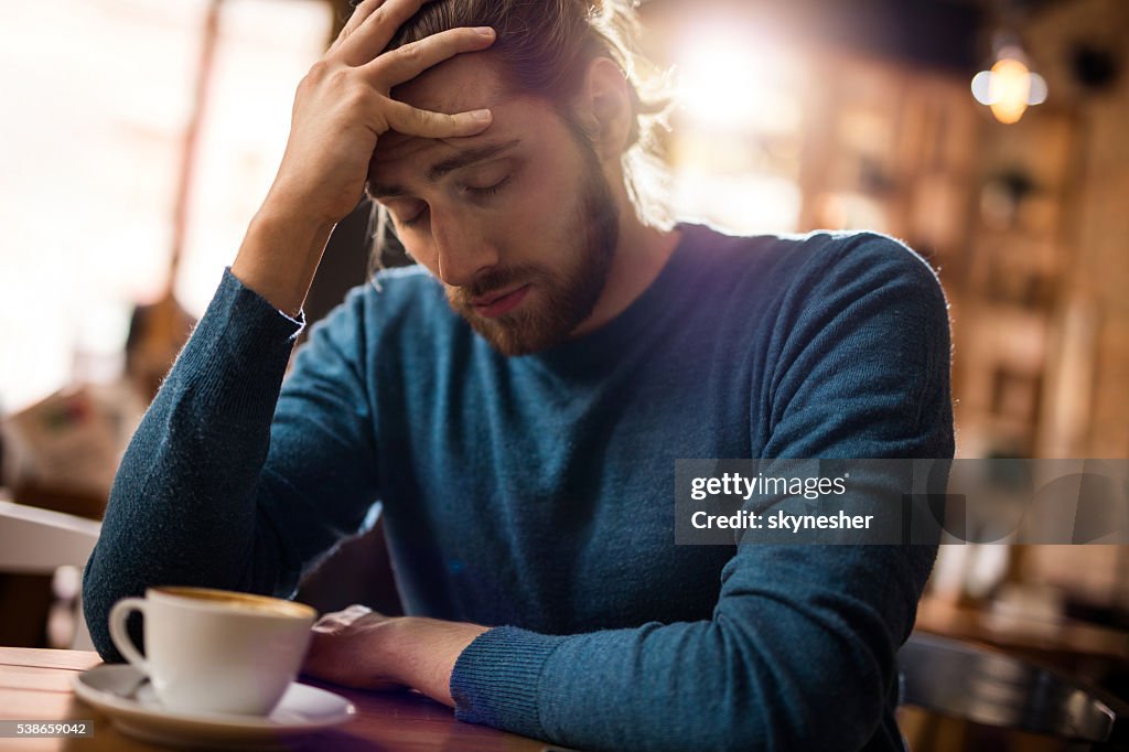 Gestresste Mann hält seinen Kopf in Schmerzen in einem Café.