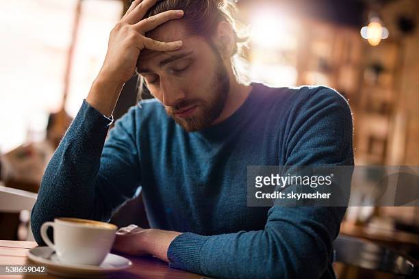 stressed man holding his head in pain in a cafe. - man headache bildbanksfoton och bilder
