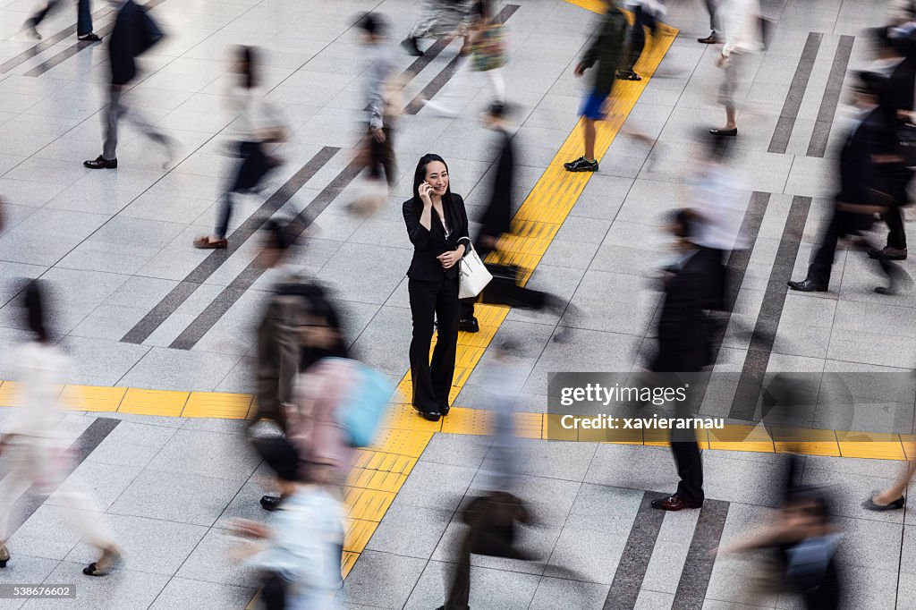 Japanese woman talking on the mobile phone surrounded by commuters