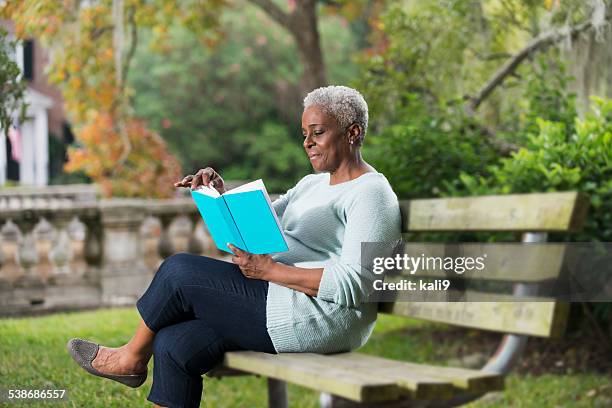 senior mujer leyendo un libro negro - mujer leyendo libro en el parque fotografías e imágenes de stock