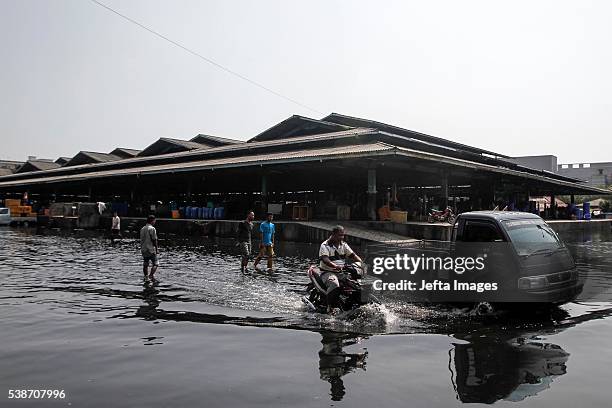 The traffic of vehicles and people passing in the tidal flood inundation in the area of the Port of Muara Baru fish market, on June 7, 2016 in...