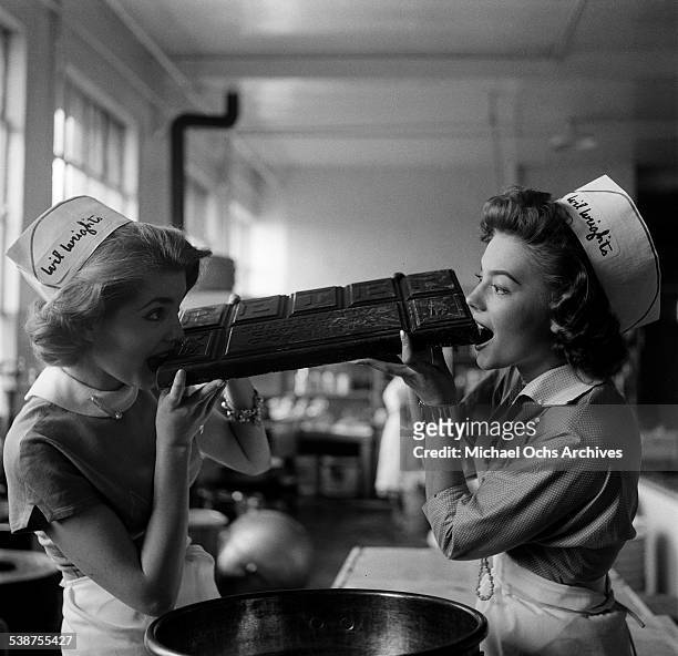 Actress Natalie Wood and actress Leigh Snowden takes a bite of a chocolate bar as they pose working at a Wil Wright's ice cream parlor in Los...