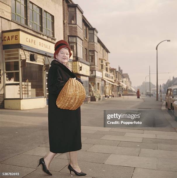 English actress Violet Carson who plays the character of Ena Sharples in the television soap opera Coronation Street, walks down a street holding a...