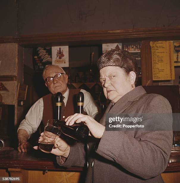 English actress Violet Carson who plays the character of Ena Sharples in the television soap opera Coronation Street, pours a glass of milk stout...