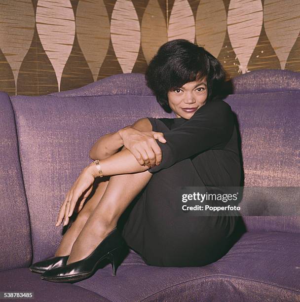 American singer and actress, Eartha Kitt pictured wearing a black dress and sitting on a couch in 1962.