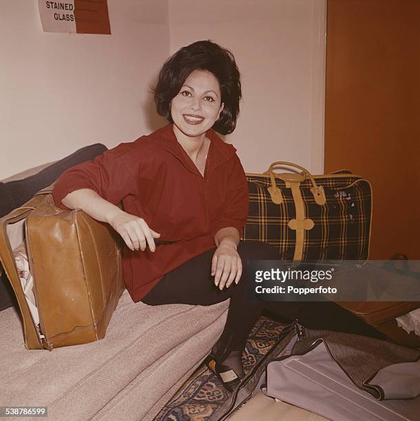 Israeli actress Haya Harareet pictured sitting on a couch surrounded by suitcases and luggage in 1962.