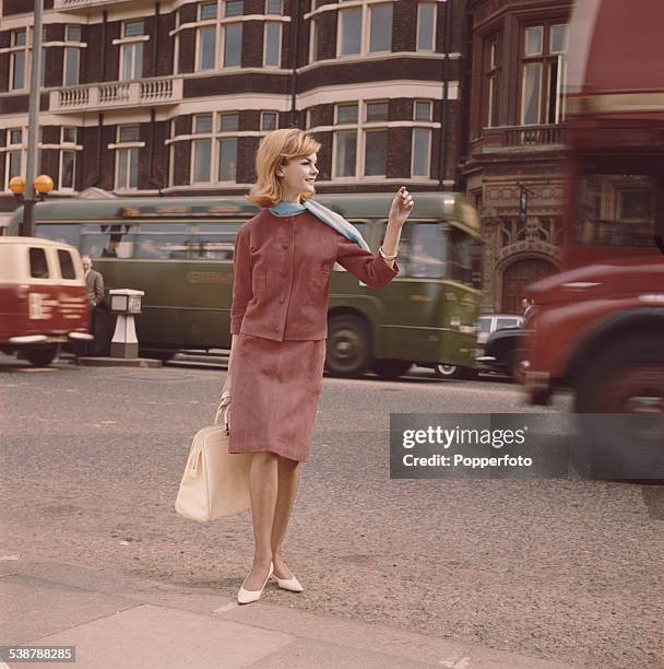 English model and actress, Jean Shrimpton pictured wearing a red suede jacket and skirt and light blue scarf whilst crossing a London street in 1962.