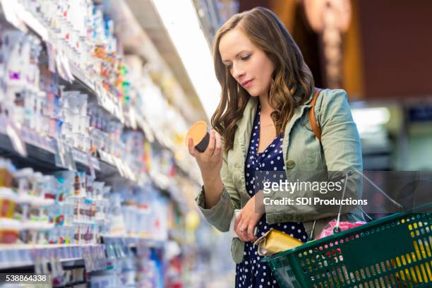 donna lettura etichette alimentari al negozio di generi alimentari - female supermarket foto e immagini stock