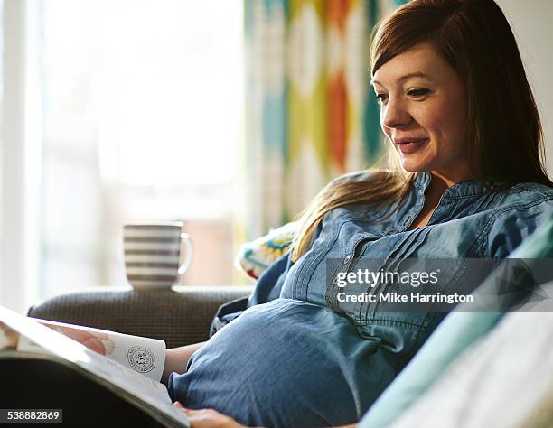 pregnant woman on sofa reading magazine. - family on couch with mugs stock-fotos und bilder