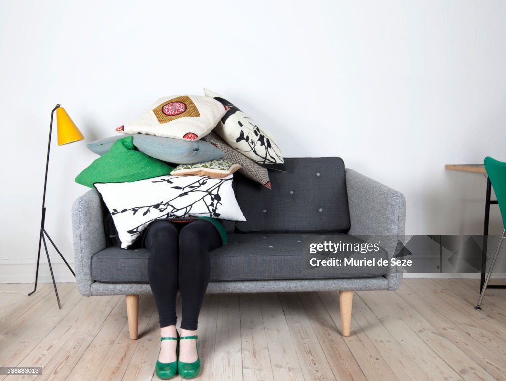 Woman sitting under pile of pillows