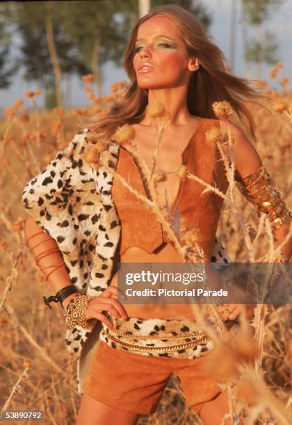 German countess and fashion model Veruschka poses in tall grass wearing a suede vest and short shorts accented by leopard printed fur, late 1960s.