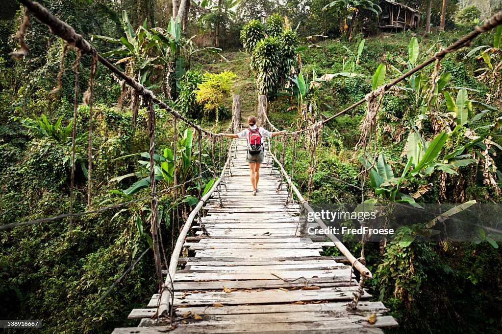 Einzelne Frau mit Rucksack auf Hängebrücke im Regenwald