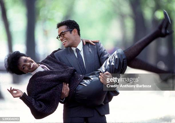 Mexican-born American actor and director Mario Van Peebles, in a grey suit, smiles as he carries an unidentified model, in a leather skirt and wool...