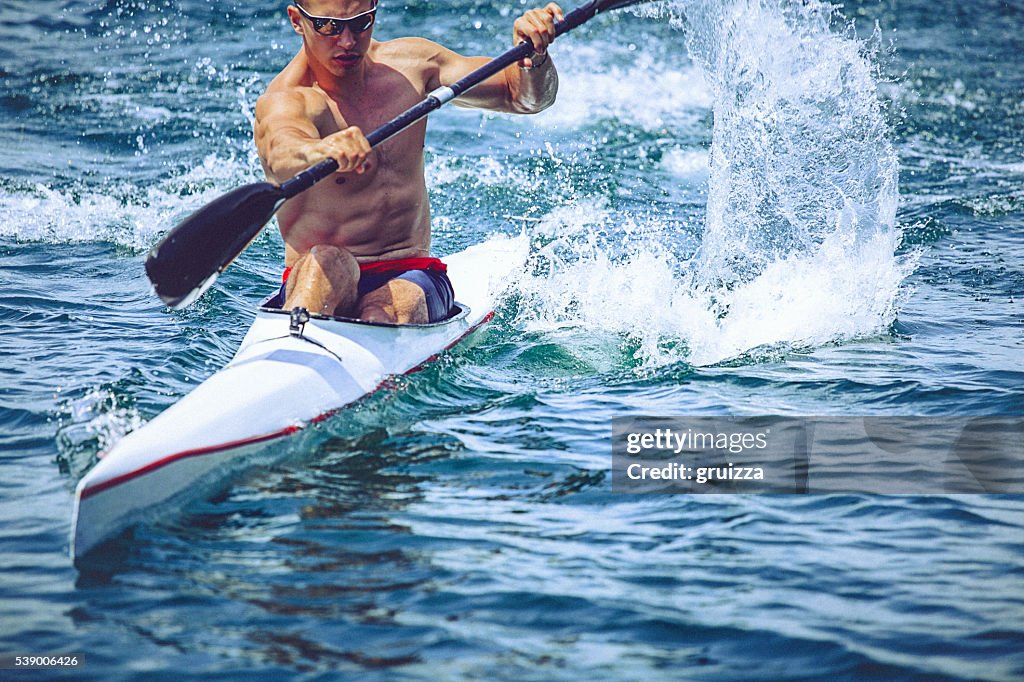 Giovane uomo muscolare in kayak sprint, alle formazione su ancora acqua.