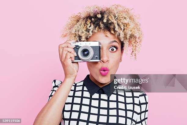 surprised young woman wearing sunglasses, holding camera - camera photographic equipment stock pictures, royalty-free photos & images
