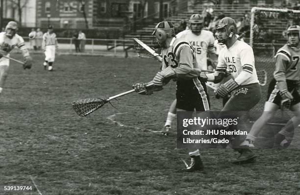 Action photograph of male Johns Hopkins University lacrosse player on the field surrounded by multiple Yale University player during a game, 1964. .