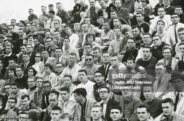 Crowd of mostly student spectators sitting in the stands, watching a Johns Hopkins University lacrosse game, 1960. .