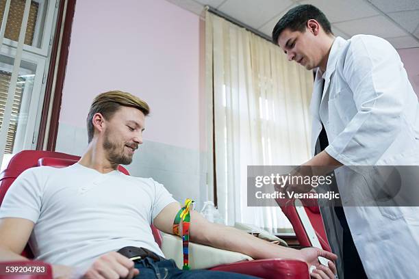 doctor preparing young man for blood donation - blood plasma stock pictures, royalty-free photos & images