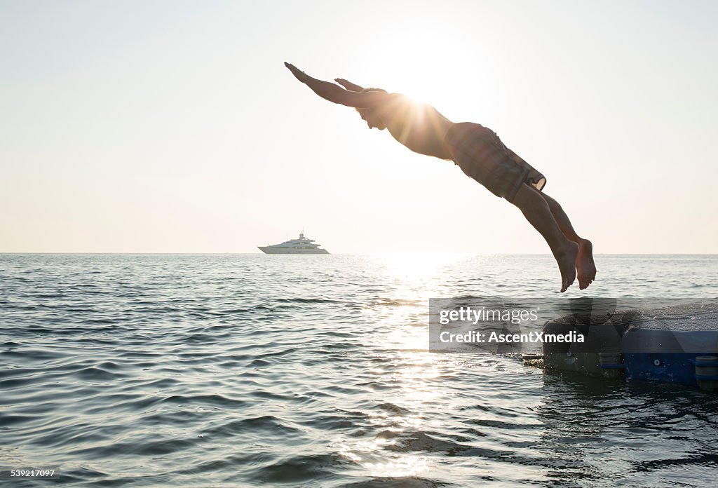 Man dives into tranquil sea, from pier, boat