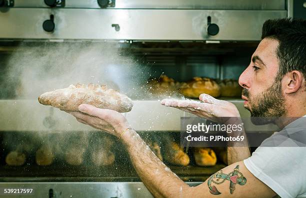 young man (baker) blows the flour on bread - beker stock pictures, royalty-free photos & images