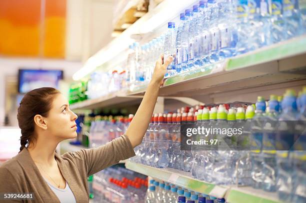 woman buys a water bottle in shop - koolzuurhoudend water stockfoto's en -beelden