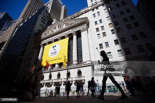 Pedestrians walk past Chine Online Education Group signage displayed outside of the New York Stock Exchange in New York, U.S., on Friday, June 10,...