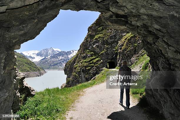 Tourist walking through cave along the Lac des Dix, formed by the Grande Dixence dam, Valais / Wallis, Swiss Alps, Switzerland.