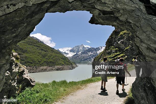 Tourists walking through cave along the Lac des Dix, formed by the Grande Dixence dam, Valais / Wallis, Swiss Alps, Switzerland.
