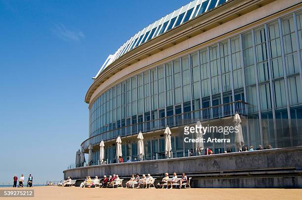 Elderly tourists sunning on sea dyke promenade behind the Casino Kursaal at seaside resort Ostend / Oostende, Belgium.
