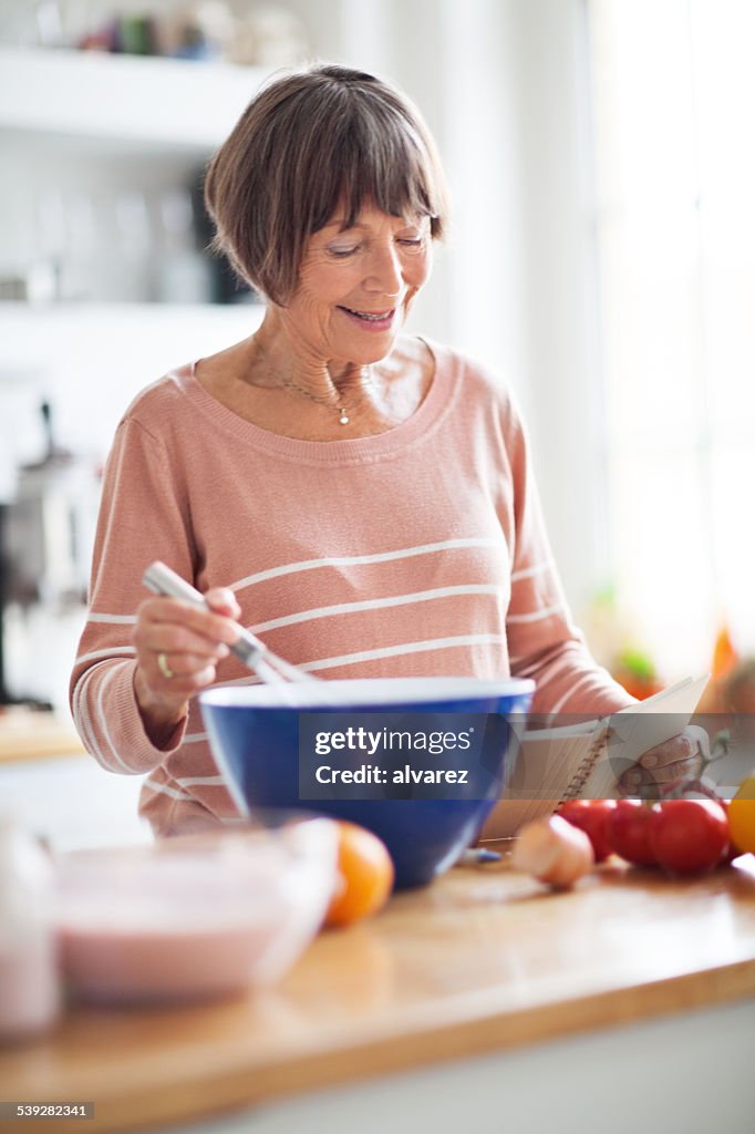 Senior woman preparing food from recipe book