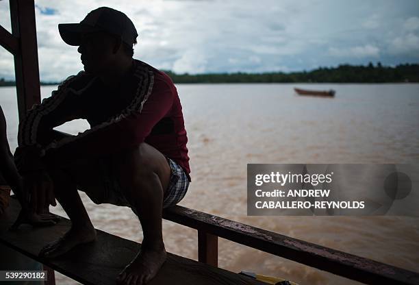 Guyanese indigenous gold miner sits on the edge of a mining barge as he watches soil pulled up from the bottom of the Mazaruni river, washed with...