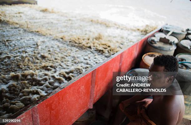Guyanese indigenous gold miner on a mining barge watches soil pulled up from the bottom of the Mazaruni river, washed with water, to separate gold...