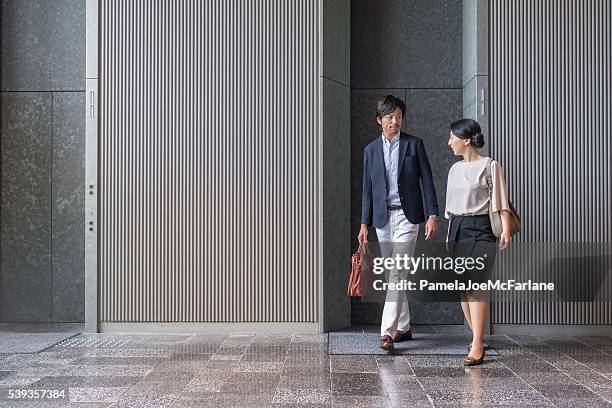 japanese businessman and businesswoman exiting elevator in modern office building - japan commuters stock pictures, royalty-free photos & images