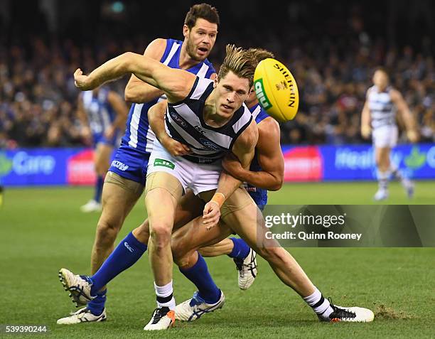 Mark Blicavs of the Cats handballs whilst being tackled by Andrew Swallow of the Kangaroos during the round 12 AFL match between the Geelong Cats and...