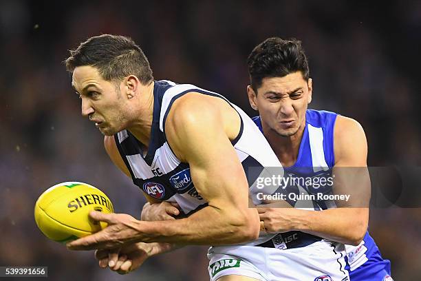 Harry Taylor of the Cats handballs whilst being tackled by Robin Nahas of the Kangaroos during the round 12 AFL match between the Geelong Cats and...