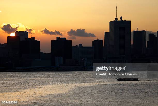 Yakatabune, or traditional low barge style boat, sails past commercial buildings on the Sumida River at dusk on June 10, 2016 in Tokyo, Japan. About...