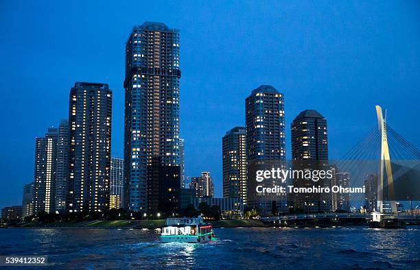 Yakatabune, or traditional low barge style boat, sails on the Sumida River as buildings stand illuminated at night on June 11, 2016 in Tokyo, Japan....